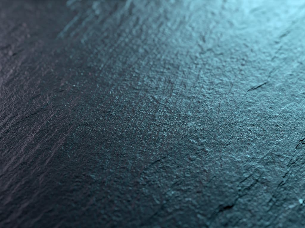 Abstract macro texture of smooth dark slate stone with fine grain under a thin wash of cool blue-teal light, no objects,